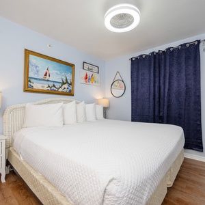The master bedroom features a comfortable bed, beach-themed decor, and a bright, cheerful atmosphere