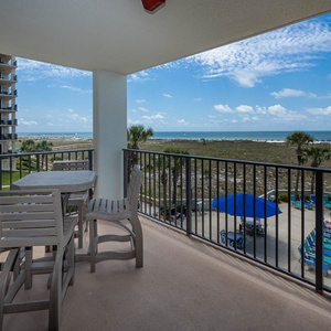 Balcony seating overlooks the beach, showcasing the gulf and pool area with lounge chairs and umbrellas for relaxation