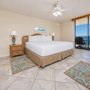Master bedroom featuring a king bed, elegant decor, and a sliding door leading to a balcony with a beach front view
