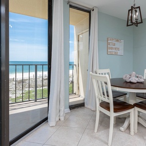 Dining area featuring a round table with four chairs, offering a view of the beach through large sliding glass doors