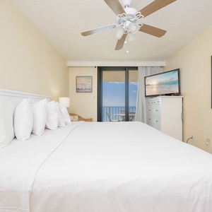Bright and airy master featuring a king bed, a TV, and a sliding door leading to the balcony with a beach front view