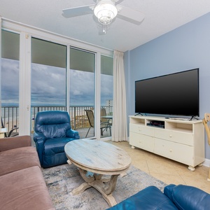 This living room features a large TV, comfortable seating, and a stunning beachfront view through expansive glass doors