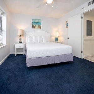 Cozy guest bedroom featuring a queen bed, plush blue carpet, and natural light from the window, creating a serene vibe