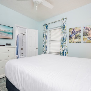 Guest bedroom featuring a queen bed, colorful artwork, a flat-screen TV, and an en-suite bathroom with a tub/shower