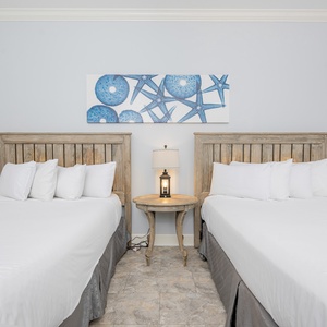 Relaxing guest bedroom featuring two cozy queen beds, beach-themed decor, and a charming nightstand with a lamp