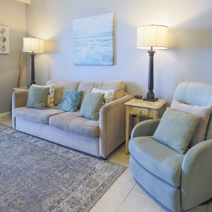 This living area features a plush sofa with decorative pillows, a cozy armchair, and soft lighting, perfect for relaxation