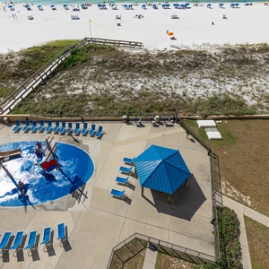 The pool area features a playful pirate ship splash park, lounge chairs, and a shaded gazebo, with a view of the beach beyond