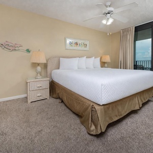 Master suite bedroom featuring a king bed, soft carpeting, and access to a balcony with views of the tranquil beach