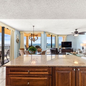 The open living area features a granite countertop, plush seating, and a view of the beach through expansive windows