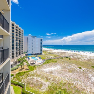 Balcony overlooks the pool area and stretches of white sand beach, framed by a vibrant blue sky and calm gulf waters