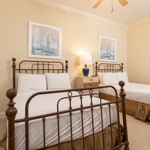 This guest bedroom features two full-size iron beds, soft beige walls, and nautical artwork, creating a serene atmosphere