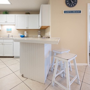 White cabinetry and a breakfast bar with stools create a welcoming space, leading to the master bedroom beyond