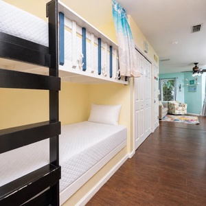 This cozy nook features a stylish bunk bed with a bright yellow wall, leading to a colorful living area beyond