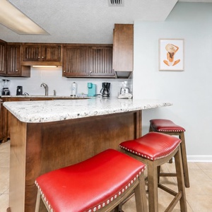 Warm wooden cabinets and red bar stools complement the granite breakfast bar in this inviting kitchen space
