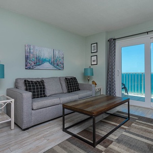 The living area features a cozy gray sofa, a stylish coffee table, and stunning beachfront views through large sliding doors