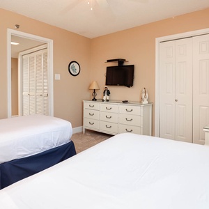 A guest bedroom features two twin beds, a dresser, a TV, and light beige walls, creating a relaxed and inviting atmosphere