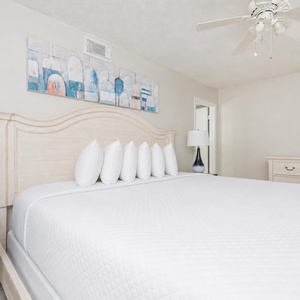 The bedroom features a large, inviting bed with white linens and decorative pillows, complemented by stylish artwork