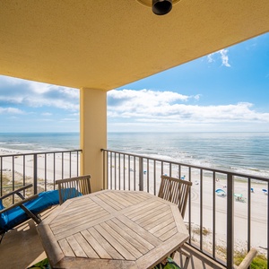 Patio table with chairs and a blue lounge chair overlooks the beach front and calm waters from the balcony