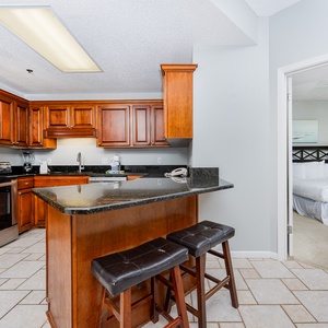 The kitchen features rich wooden cabinetry, a breakfast bar with seating, and a view into the cozy master suite