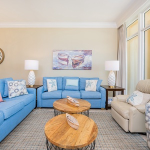 Relax in the airy living room, featuring comfortable blue seating, coastal decor, and beachfront balcony access