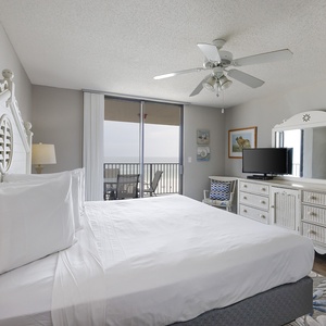 Bright master bedroom featuring a king bed, a TV, and sliding glass doors leading to a balcony with a beach front view