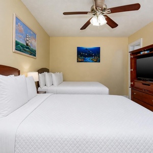 This guest bedroom features two comfortable beds, a TV, and vibrant ocean-themed artwork for a relaxing stay