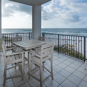 This balcony features a dining table and chairs overlooking the pool area, perfect for enjoying beach views and relaxing