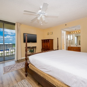 Master bedroom featuring a king bed, a flat-screen TV, and the balcony view with light curtains framing the outdoors