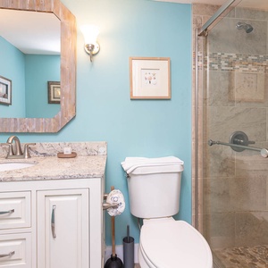 The bathroom features a granite countertop, spacious glass shower, and calming turquoise walls for a refreshing retreat