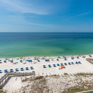 The image showcases a vibrant beach scene with colorful umbrellas and people enjoying the sun on white sand