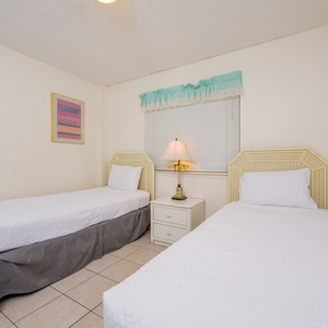 This bright room features two twin beds, colorful artwork, and a cozy lamp, perfect for a restful stay