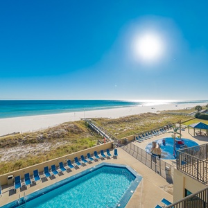 Sparkling pool area with lounge chairs, leading to a pristine beach and vibrant blue waters under a sunny sky