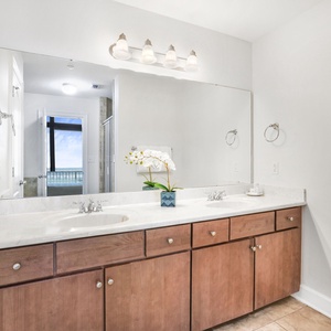 The master bath features a double vanity with wood cabinetry, elegant lighting, and a view of the beach through the window