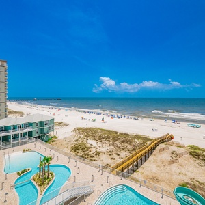 Enjoy the vibrant view from your balcony, showcasing the inviting pool area and beach under a clear blue sky