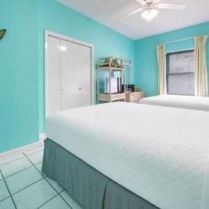 Bright turquoise walls complement two queen beds and a TV stand, creating a cheerful atmosphere in this inviting guest room