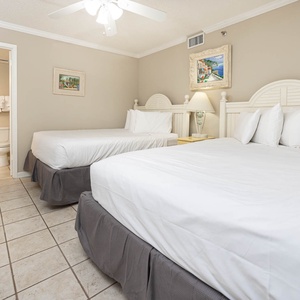 Rest comfortably in this guest bedroom, featuring two queen beds, soft linens, and charming artwork on the walls