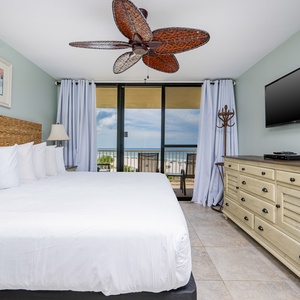 The master bedroom features a king-size bed, a TV, and a stunning beachfront view through sliding glass doors