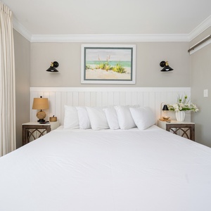 Elegant master bedroom featuring a plush white king bed, stylish lamps, and beach-themed artwork for a relaxing getaway