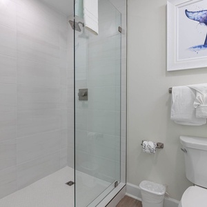 This bathroom features a glass walk-in shower, fresh towels, and a charming whale art piece, perfect for a refreshing retreat