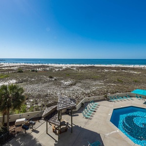 Expansive beach view showcases the pool area with lounge chairs and a gazebo, framed by white sand and blue gulf waters