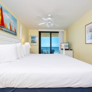 Master bedroom featuring a king bed, a TV, and a balcony with a view of the tranquil beachfront