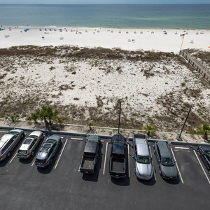 This view showcases a serene beachfront with white sand and beachgoers, complemented by a nearby inviting swimming pool