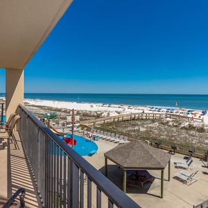 The balcony features a dining table with chairs, offering a second floor view of the beach, pool area, and pirate splash park
