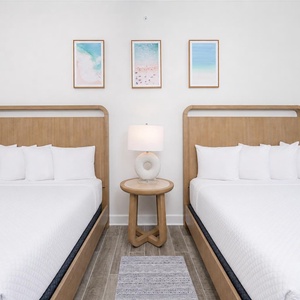Inviting guest bedroom featuring two comfortable queen beds, a stylish lamp, and coastal artwork