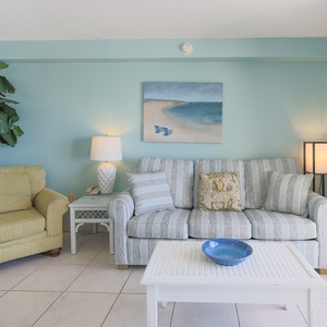 The living area features a light blue color scheme, a cozy striped sofa, and a vibrant beach painting, perfect for relaxation