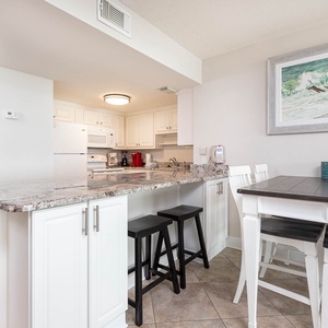 This kitchen features sleek white cabinetry, granite countertops, and a cozy dining area with a stylish table and chairs
