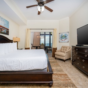 The master bedroom features a plush king bed, a large TV, and a serene view through sliding glass doors to the balcony