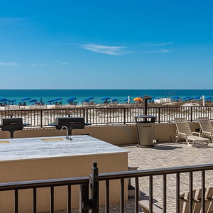 Outdoor balcony patio overlooking the grilling station and pool area surrounded by loungers and the beach beyond