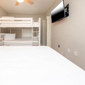 Cozy guest bedroom featuring a queen bed, a bunk bed with two queens, and a flat-screen TV for entertainment