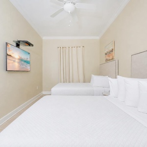Soothing guest bedroom featuring two queen beds, soft linens, and a mounted TV